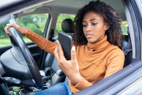 Young woman checks her cell phone while driving