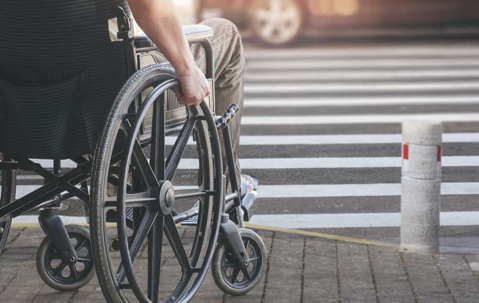 Man sits in a wheelchair waiting to cross the street at an intersection