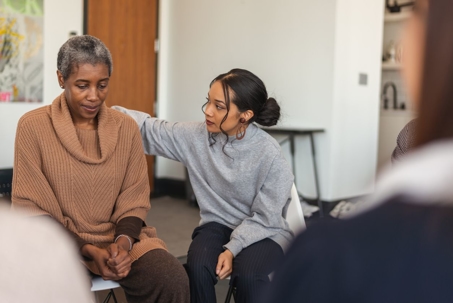 Young woman comforting older woman in support group.